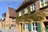Ockerfarbene Idylle: Grüner Wilder Wein rankt an der historischen Häuserzeile mit den grünen Türen.